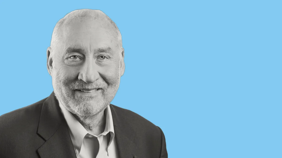 A black and white portrait shows Joseph Stiglitz, an older white man with a bald head and a short, light-colored beard, smiling slightly against a light blue background.
