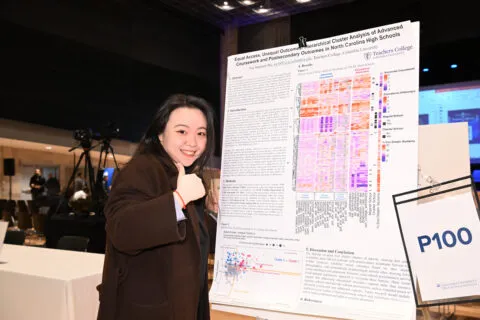Student gives thumbs up in front of her research poster