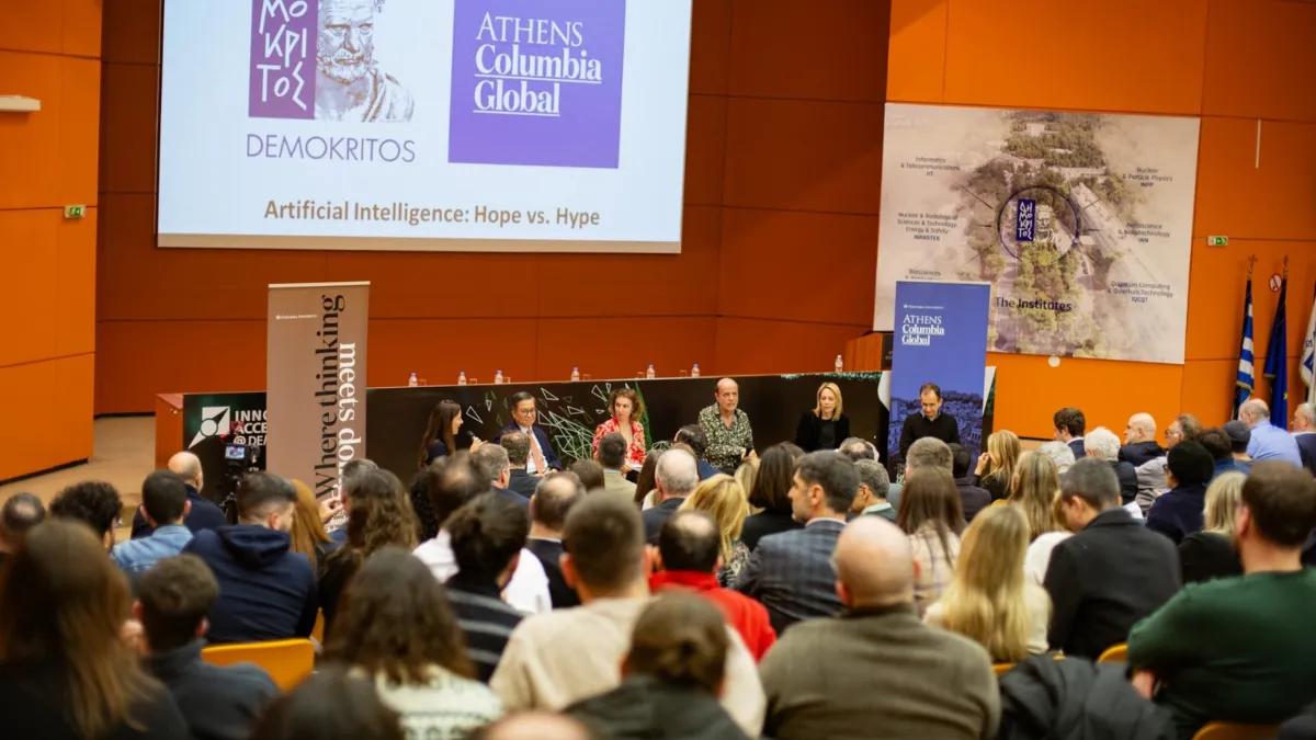 A panel discussion on “Artificial Intelligence: Hope vs. Hype” at a Columbia Global event in Athens, with speakers seated at a long table and a large audience in attendance.