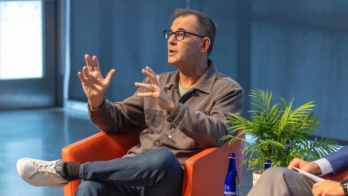 Intrator, seated in an orange chair gestures expressively while speaking during a panel discussion.