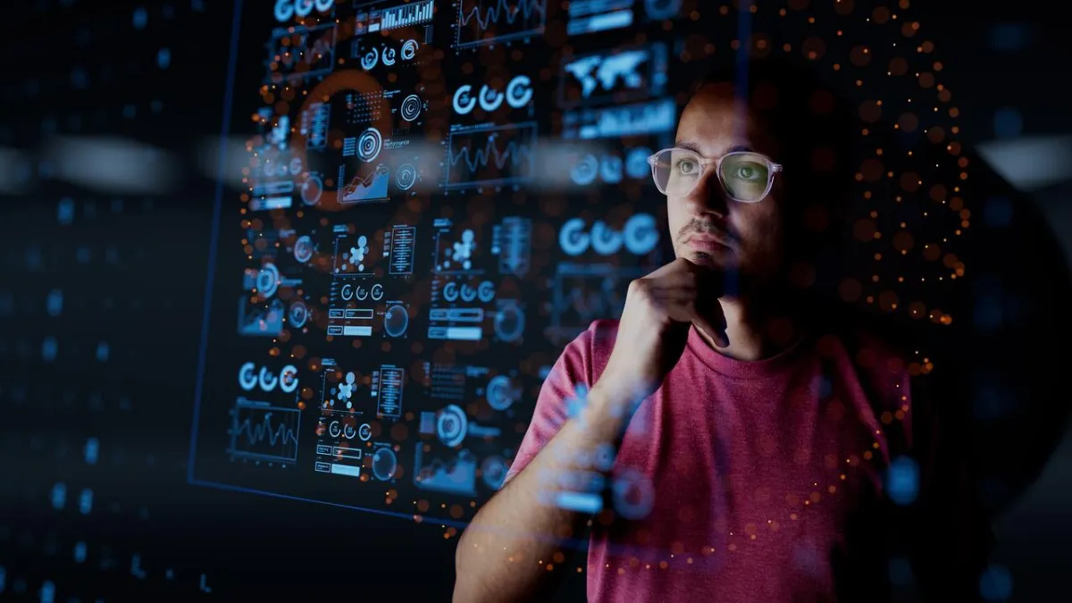 A man wearing glasses and a red t-shirt looks thoughtfully at a transparent digital interface displaying data visualizations, graphs, and analytics, symbolizing AI-driven insights and decision-making.