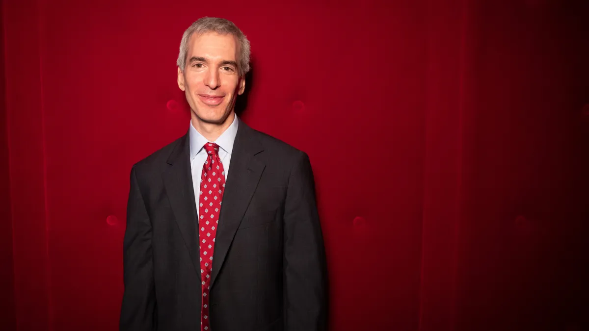 Jeremy Caplan, a journalism teacher and newsletter author, pictured against a red wall. 