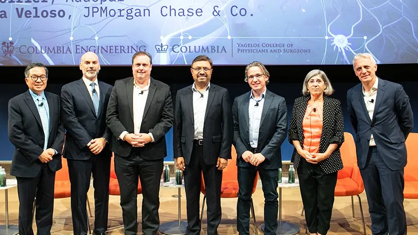 Seven panelists, six male and one female, stand on stage to pose for a photo.